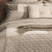 Close-up of Panorama patchwork quilt in natural, ivory and taupe with quilted stitching and a striped reverse folded back
